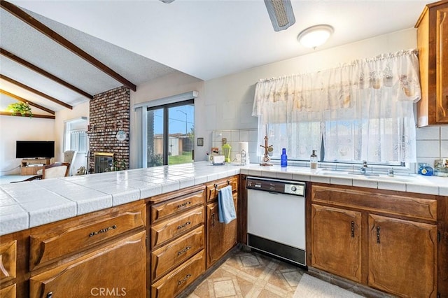 kitchen with tile countertops, white dishwasher, lofted ceiling with beams, sink, and a brick fireplace