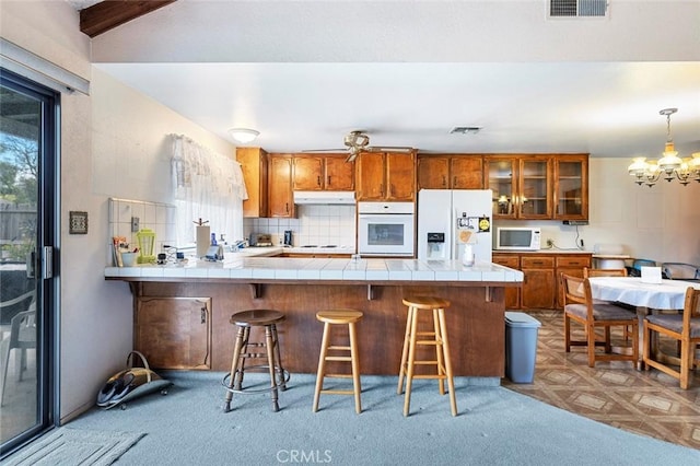 kitchen featuring white appliances, an inviting chandelier, hanging light fixtures, tile counters, and kitchen peninsula