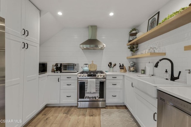 kitchen with appliances with stainless steel finishes, white cabinetry, island range hood, sink, and light hardwood / wood-style flooring