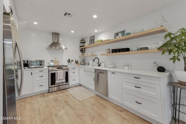 kitchen featuring wall chimney range hood, stainless steel appliances, white cabinetry, and sink