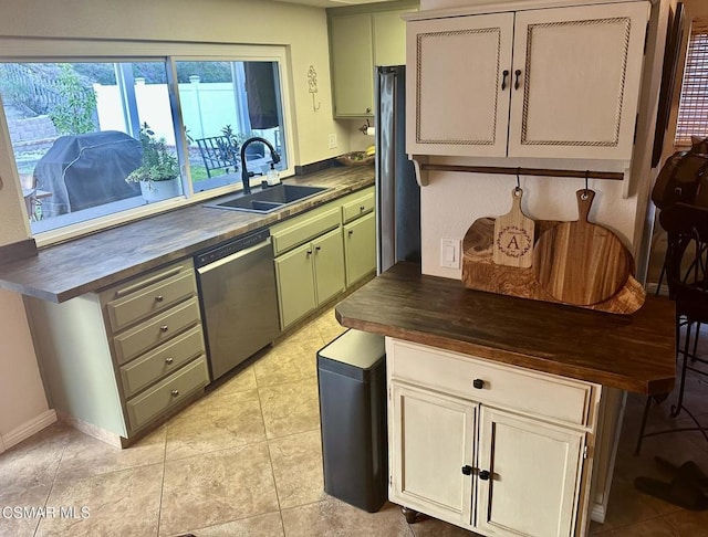 kitchen featuring sink, light tile patterned floors, dishwasher, butcher block countertops, and green cabinets