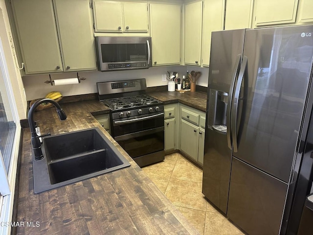 kitchen with green cabinets, sink, light tile patterned floors, and stainless steel appliances