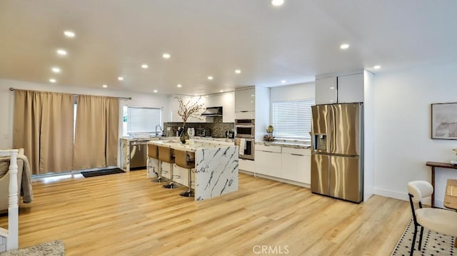 kitchen with a breakfast bar, stainless steel appliances, white cabinetry, and light hardwood / wood-style flooring