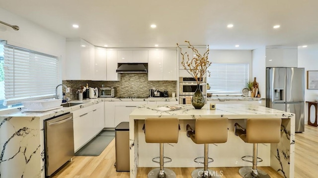 kitchen with white cabinets, light wood-type flooring, stainless steel appliances, and extractor fan