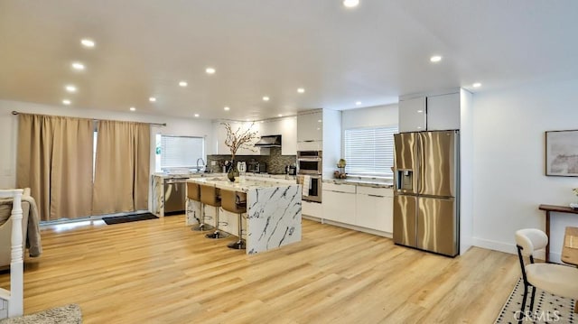 kitchen featuring white cabinetry, a breakfast bar, stainless steel appliances, and light wood-type flooring