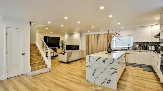 kitchen featuring white cabinets, sink, light wood-type flooring, a kitchen island, and a tiled fireplace