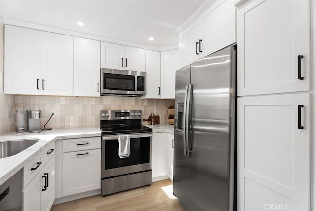 kitchen with decorative backsplash, light hardwood / wood-style flooring, white cabinets, and appliances with stainless steel finishes