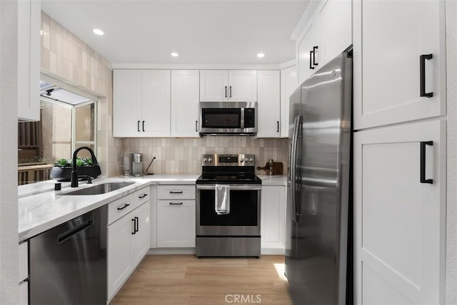 kitchen featuring white cabinetry, sink, stainless steel appliances, light hardwood / wood-style flooring, and decorative backsplash