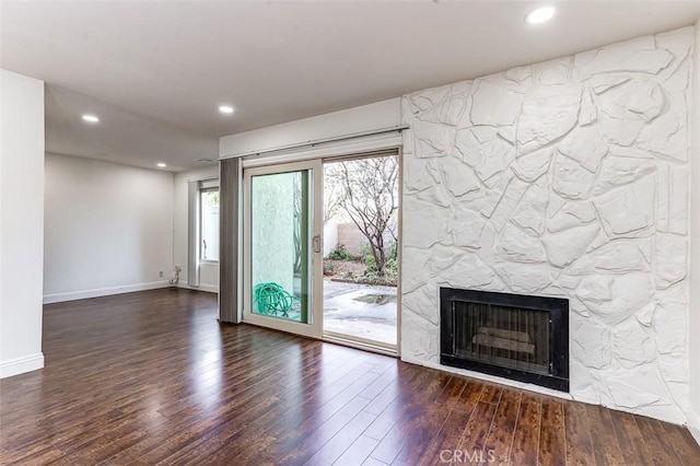 unfurnished living room featuring dark wood-type flooring and a stone fireplace