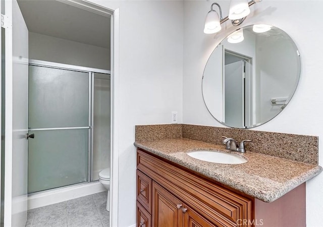 bathroom featuring a shower with shower door, toilet, vanity, and tile patterned flooring