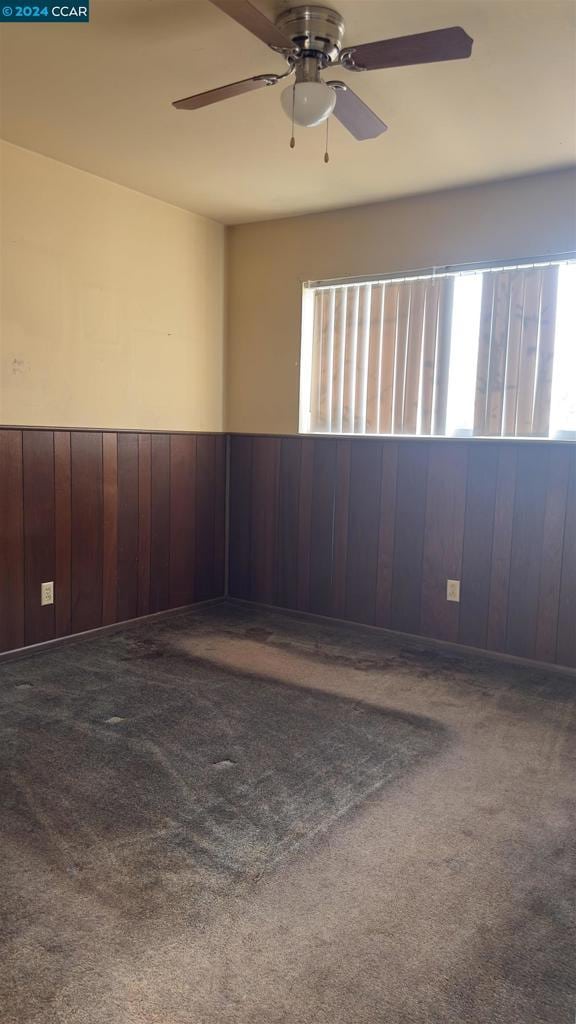 carpeted spare room with ceiling fan and wood walls