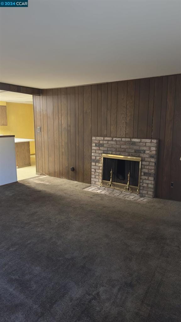 unfurnished living room featuring carpet flooring, a brick fireplace, and wood walls