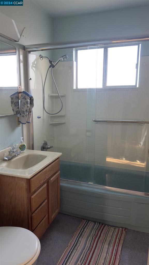 full bathroom with vanity, a healthy amount of sunlight, toilet, and bath / shower combo with glass door