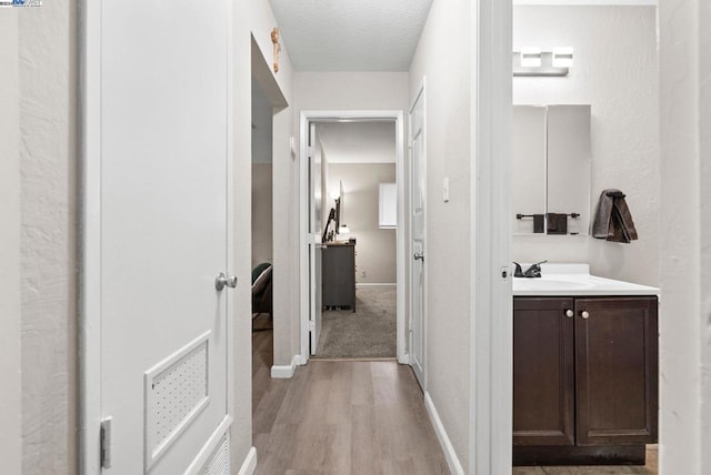 hallway with a textured ceiling, light hardwood / wood-style floors, and sink