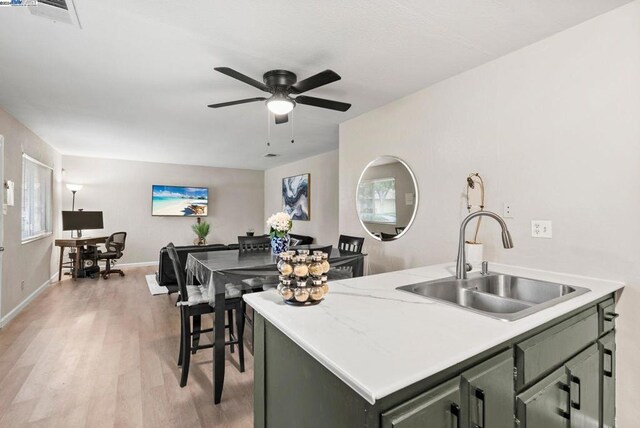 kitchen with green cabinets, sink, light hardwood / wood-style flooring, ceiling fan, and an island with sink