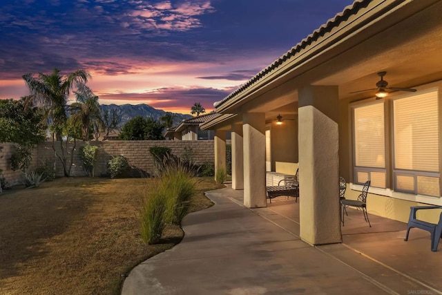 patio terrace at dusk featuring a mountain view and ceiling fan