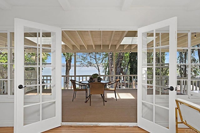 sunroom with beam ceiling, french doors, and a water view