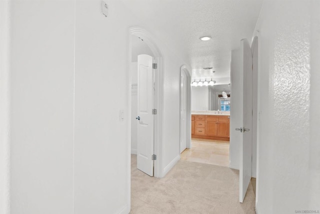 hallway featuring a textured ceiling and light colored carpet