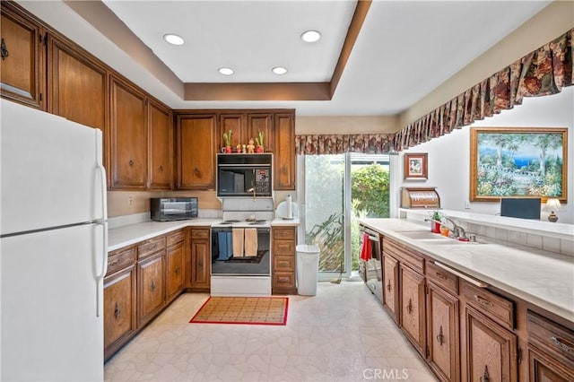 kitchen featuring white appliances, sink, and a tray ceiling