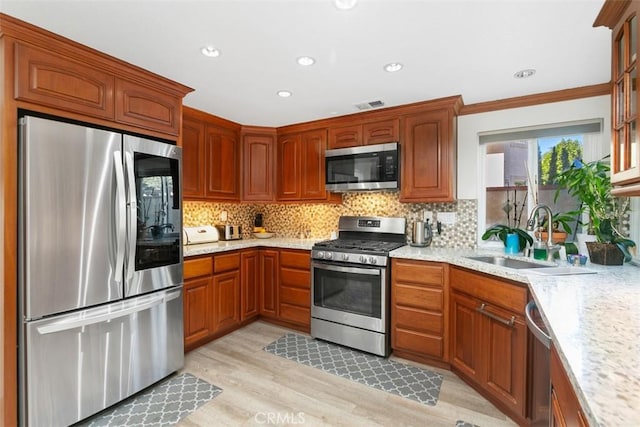 kitchen featuring appliances with stainless steel finishes, sink, light stone counters, light wood-type flooring, and decorative backsplash