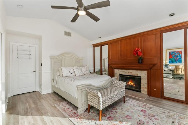 bedroom with light hardwood / wood-style floors, lofted ceiling, ceiling fan, and a fireplace