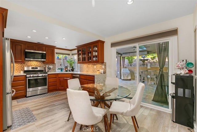 kitchen with decorative backsplash, stainless steel appliances, light stone counters, and light hardwood / wood-style flooring