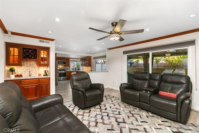 living room with ceiling fan, indoor wet bar, light hardwood / wood-style floors, and crown molding