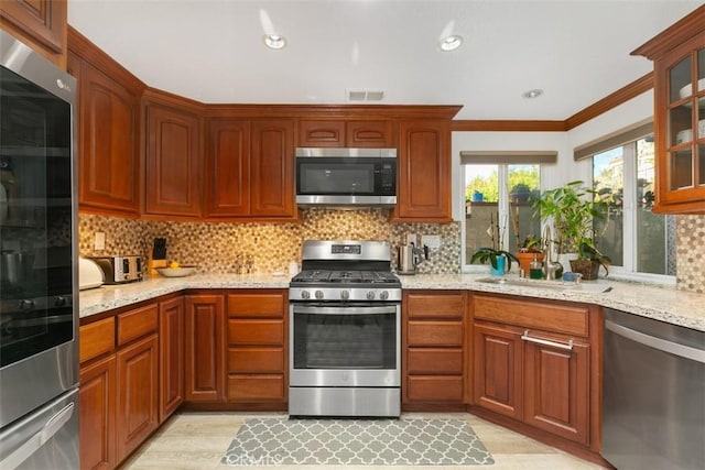 kitchen with tasteful backsplash, stainless steel appliances, light stone countertops, crown molding, and sink