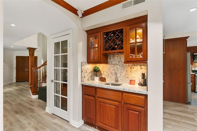 bar with sink, light hardwood / wood-style floors, crown molding, light stone countertops, and decorative backsplash