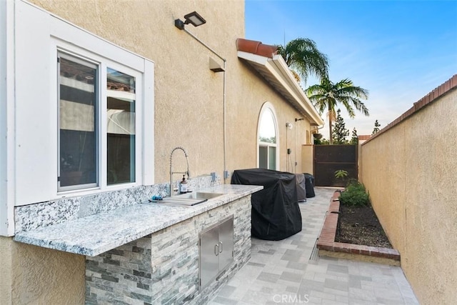 patio terrace at dusk featuring an outdoor wet bar, exterior kitchen, and grilling area