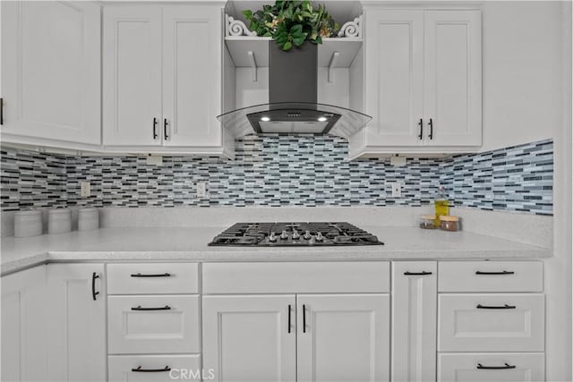 kitchen with stainless steel gas cooktop, backsplash, white cabinets, and wall chimney range hood