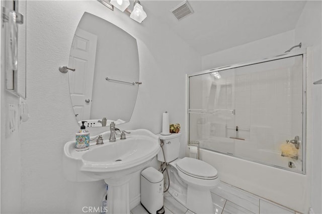 full bathroom featuring sink, bath / shower combo with glass door, and toilet