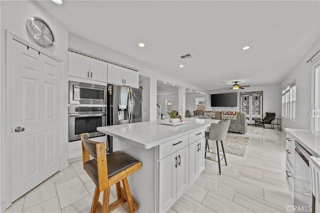 kitchen with ceiling fan, a breakfast bar, white cabinets, and stainless steel appliances