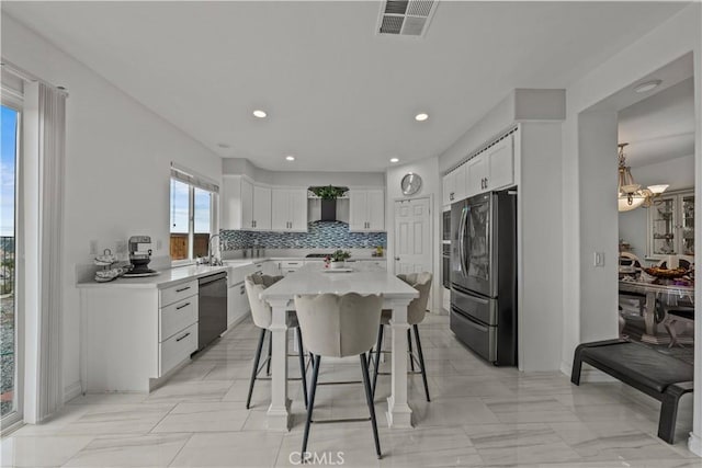 kitchen with a kitchen island, decorative backsplash, white cabinetry, appliances with stainless steel finishes, and a breakfast bar area