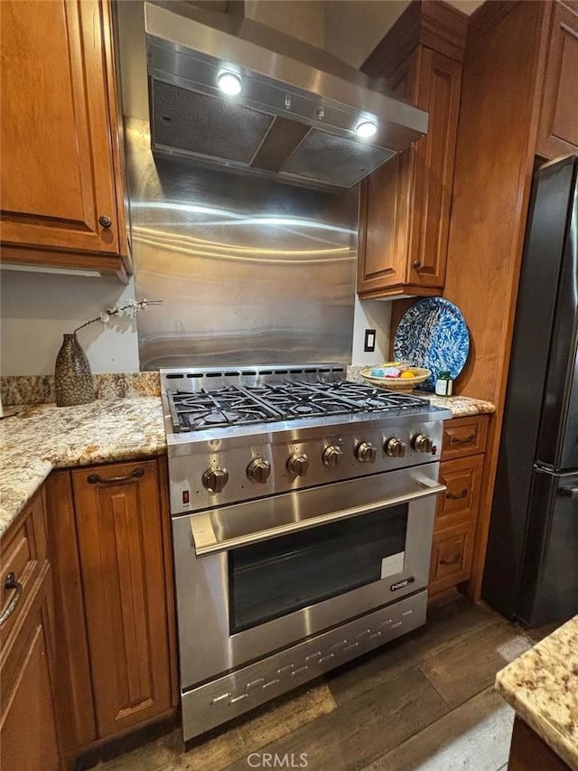 kitchen featuring stainless steel range, black fridge, dark hardwood / wood-style flooring, wall chimney range hood, and light stone counters