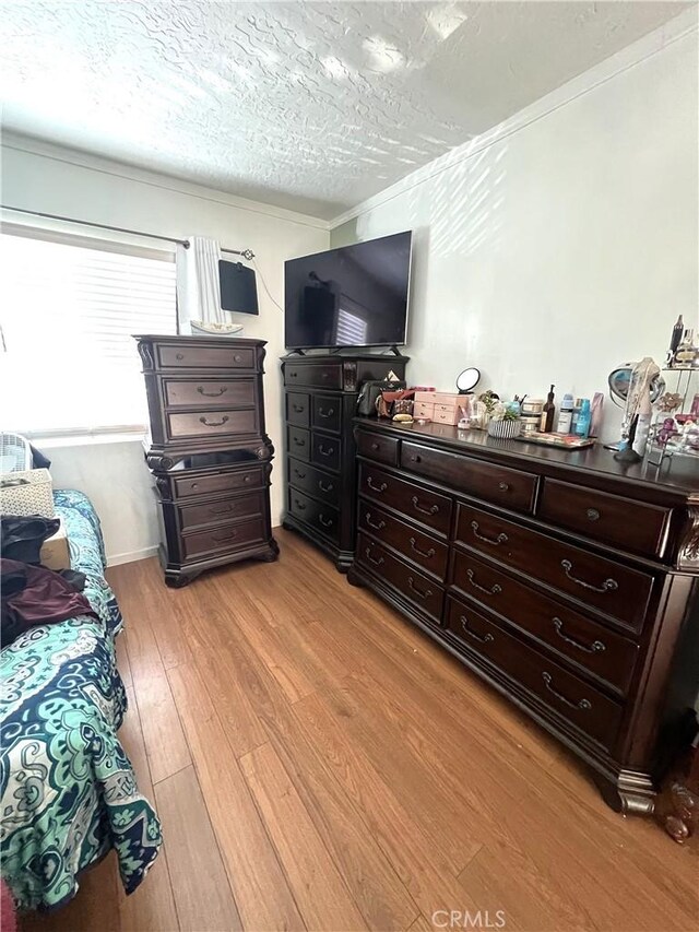 bedroom featuring a textured ceiling, light wood-type flooring, and crown molding