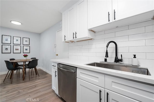 kitchen with sink, light hardwood / wood-style flooring, white cabinetry, decorative backsplash, and stainless steel dishwasher
