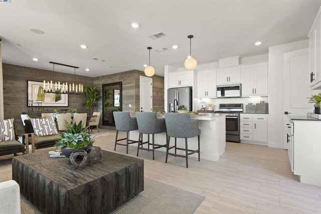 living room with wood walls, light hardwood / wood-style floors, and an inviting chandelier