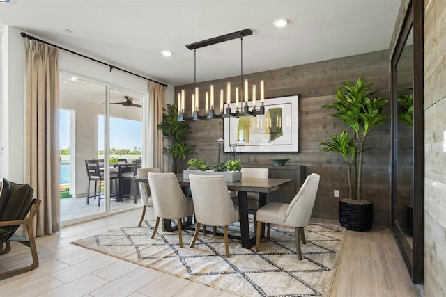 dining room with a chandelier, light wood-type flooring, a water view, and wood walls