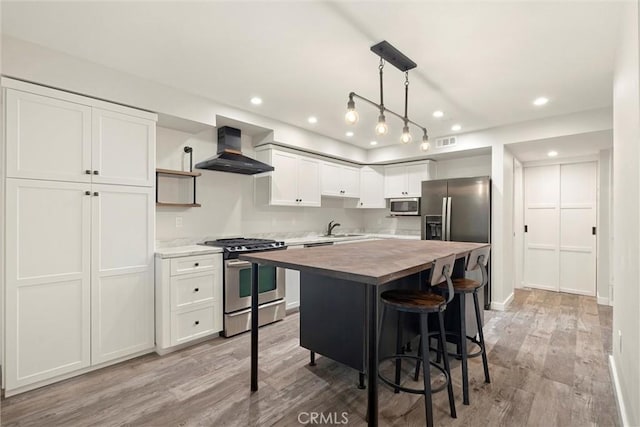 kitchen with wall chimney exhaust hood, hanging light fixtures, wood counters, white cabinets, and appliances with stainless steel finishes