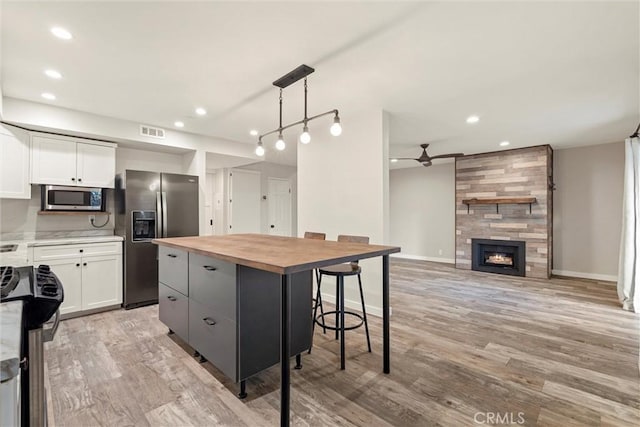 kitchen featuring white cabinets, decorative light fixtures, a center island, and stainless steel appliances