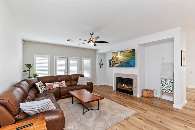 living room featuring light hardwood / wood-style flooring, ceiling fan, and a tiled fireplace