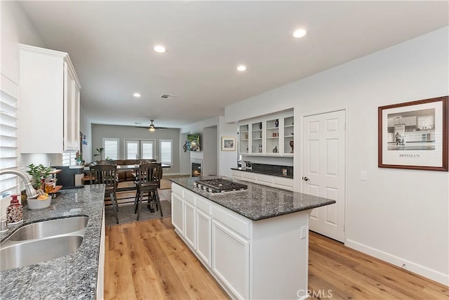 kitchen featuring stainless steel gas stovetop, white cabinets, sink, light hardwood / wood-style flooring, and a kitchen island