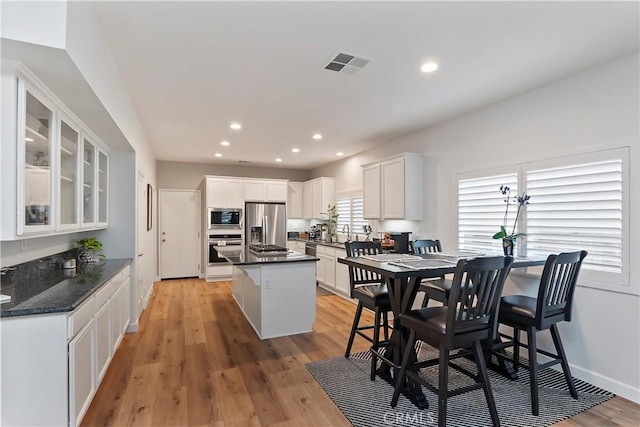 kitchen with white cabinets, a center island, light wood-type flooring, and stainless steel appliances