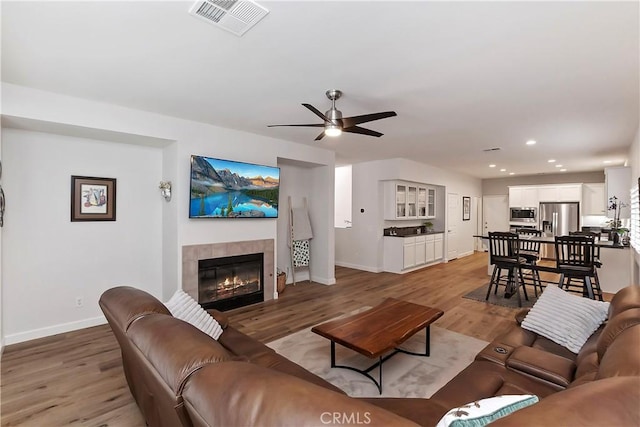 living room featuring a tile fireplace, light hardwood / wood-style flooring, and ceiling fan