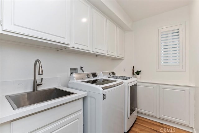 laundry room featuring washer and clothes dryer, light hardwood / wood-style floors, cabinets, and sink