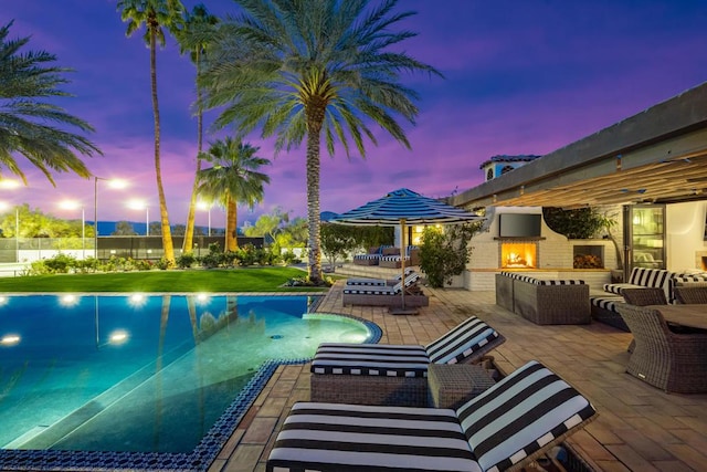 pool at dusk with a patio area and exterior fireplace