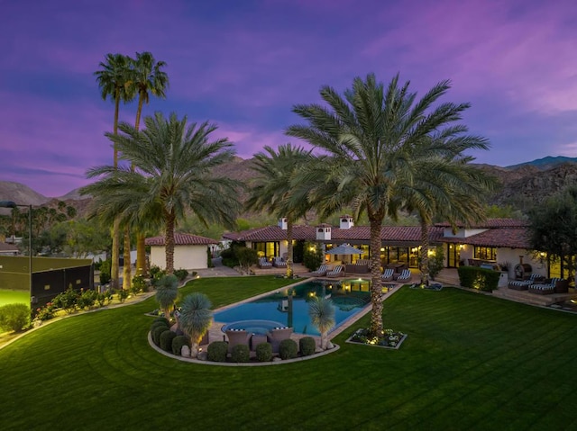 pool at dusk featuring a mountain view, a patio area, and a lawn