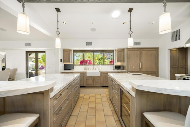 kitchen with a large island, light stone counters, sink, and hanging light fixtures