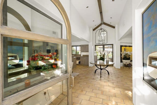 interior space with light tile patterned flooring, beamed ceiling, a chandelier, and high vaulted ceiling